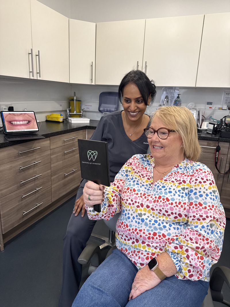 Radhika showing a patient her finished smile in a hand mirror at Dentistry @ Jordanhill